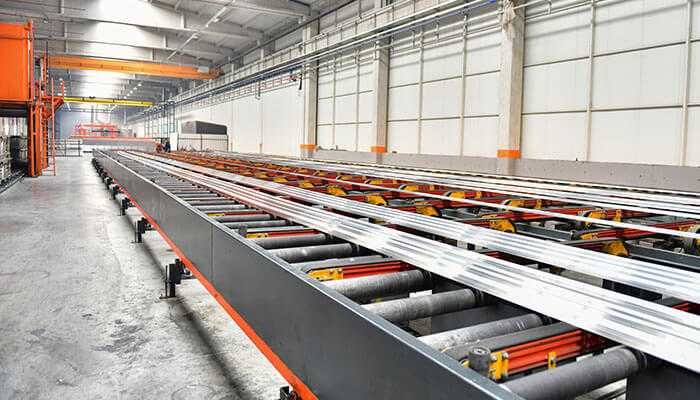 Efficient material utilization - tycoonstory | tycoonstory media A manufacturing facility showcasing a profile extrusion line with long metal profiles on conveyor belts, illustrating the precision and efficiency of the extrusion process in modern manufacturing