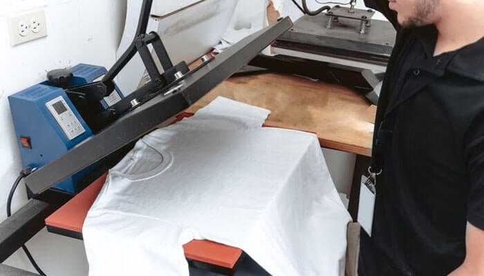 Ignoring temperature and pressure settings - tycoonstory | tycoonstory media Person operating a custom screen print transfers to print a design on a white t-shirt in a printing studio.