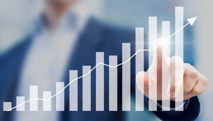 Improved efficiency and productivity- tycoonstory | tycoonstory media A person in a business suit pointing at a rising bar graph with an upward trend line, symbolizing growth, success, and financial or business progress