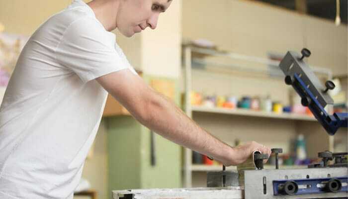 Integration with digital workflows - tycoonstory | tycoonstory media Person at work on a screen dtf printing machine in a workshop, printing on textiles and papers.