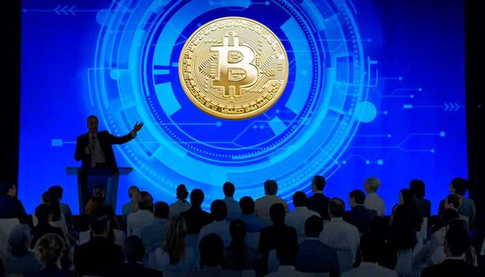Leverage conference resources - tycoonstory | tycoonstory media A person presenting a bitcoin investmrnt conference with a bitcoin symbol background along with wider audience