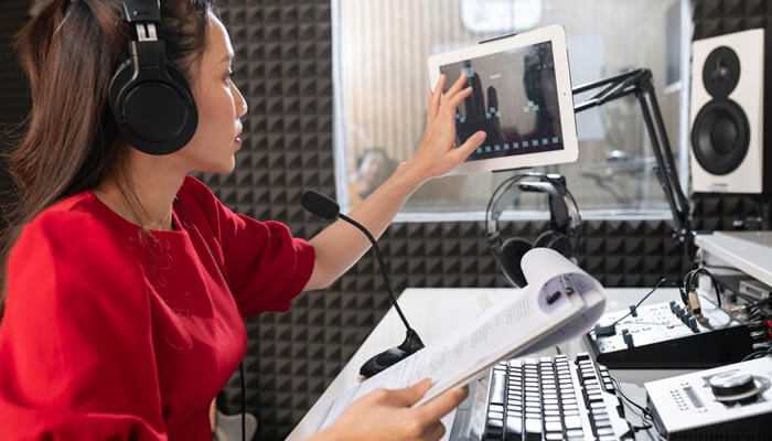 Maintaining a schedule - tycoonstory | tycoonstory media The radio broadcaster with online radio software on the tablet and speaking into a microphone in a studio.