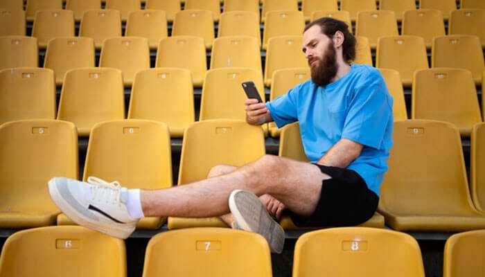 Social media integration- tycoonstory | tycoonstory media A man watching cricket on his smartphone in an empty stadium, symbolizing how mobile apps are transforming cricket viewing by bringing the game to any location