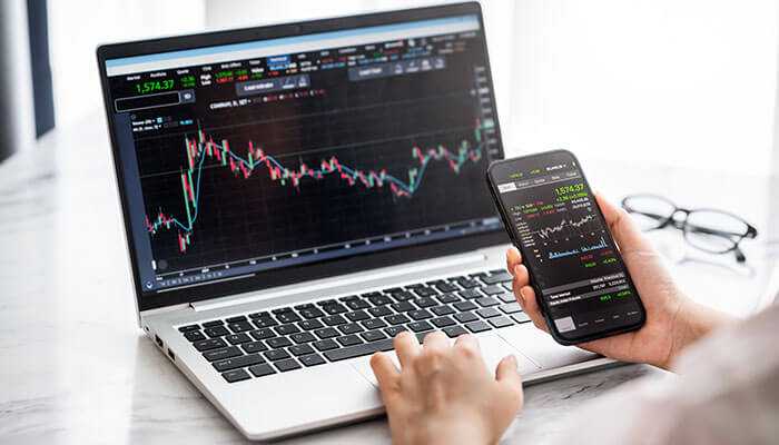 Spread betting- tycoonstory | tycoonstory media An image of a person using a laptop and smartphone to monitor cfd trading charts, highlighting real-time market data and trends in cfd trading vs financial spread betting