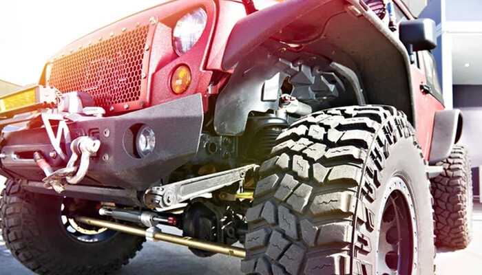 Red off-road vehicle with suspension lift kit and rugged tires, highlighting nissan frontier accessories for tough terrains Off-road vehicle with rugged tires and suspension parts showcasing heavy-duty nissan frontier accessories.