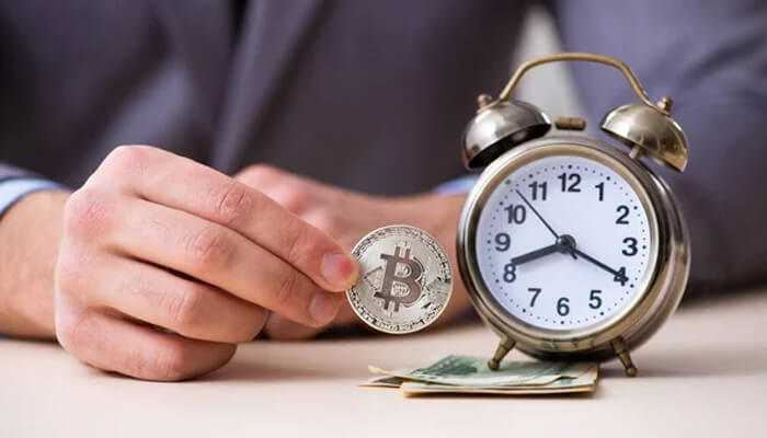 Timing the market - tycoonstory | tycoonstory media Person holding a bitcoin coin next to an analog clock and cash to represent the concept of the best time to buy cryptocurrency.