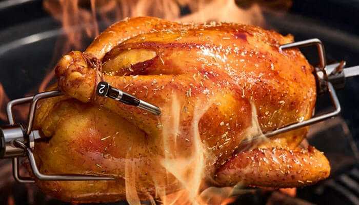 Typhur sync gold dual - tycoonstory | tycoonstory media Close-up of a whole chicken roasting on a rotisserie with a wireless meat thermometer probe inserted, surrounded by flames.