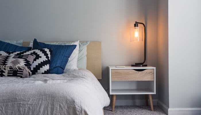 Understanding the impact of bed bugs - tycoonstory | tycoonstory media Modern hotel room with a neatly made bed and a bedside table with a lamp showcasing a clean environment essential for bed bugs prevention in the hospitality industry