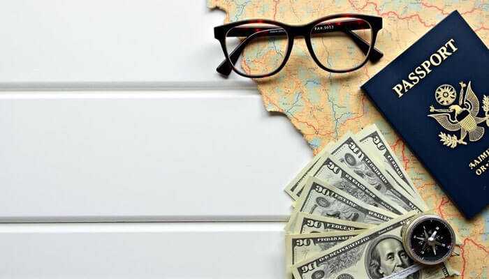 Vietnam visa charges for indian citizens - tycoonstory | tycoonstory media Travel essentials including glasses, a passport, cash in various denominations, a map, and a compass, symbolizing adventure and international travel.