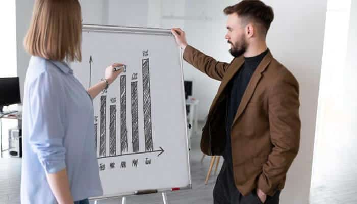 A necessary element for predictable corporate growth - tycoonstory | tycoonstory media Professionals discussing a whiteboard bar chart to represent analytics driven with the help of small business it services.