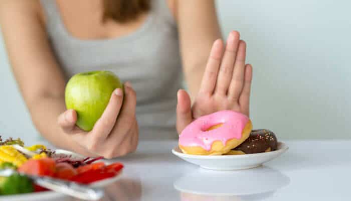 An appetite for eating-oriented stocks - tycoonstory | tycoonstory media A person making a health-conscious choice between an apple and donuts, symbolizing the discipline and decision-making required in hedge fund investments.