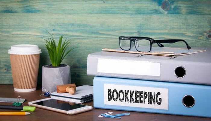 Best bookkeeping practices - tycoonstory | tycoonstory media Organized workspace on a wooden desk with bookkeeping files, spectacles, smartphone, coffee mug, and office supplies.