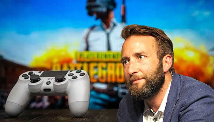Brendan greene - tycoonstory | tycoonstory media Brendan greene, creator of pubg, with a gaming controller in focus, representing success stories of entrepreneurs in the gaming sector