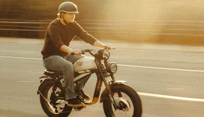 Built for adult comfort and convenience - tycoonstory | tycoonstory media Man riding an electric bike on a city street during sunset, wearing a helmet, illustrating the convenience and style of urban commuting with eletric bikes