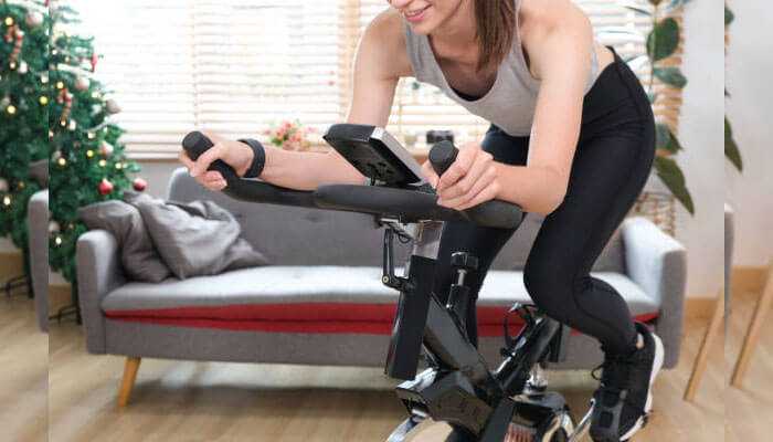 Built-in technology and monitoring - tycoonstory | tycoonstory media A woman exercising in her home in a cozy living room with holiday decorations represents home exercise bikes for exercise.