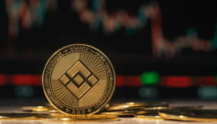 Challenges and risks associated with bnb - tycoonstory | tycoonstory media Close-up of the binance cryptocurrency coin with a blurred stock market chart in the background, symbolizing digital asset trading.