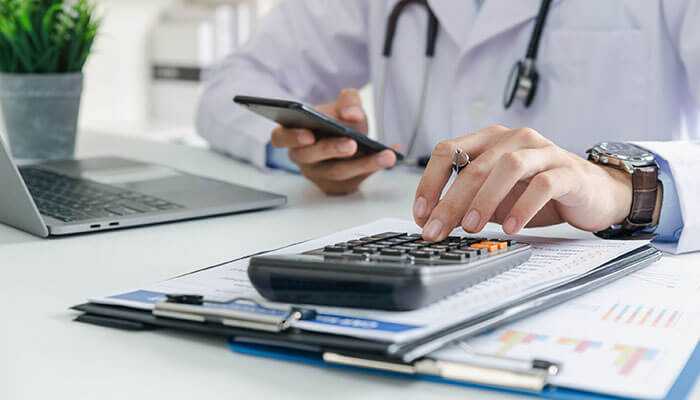 Determining payment amounts - tycoonstory | tycoonstory media Healthcare professional using a calculator and reviewing documents while a doctor in a white coat analyzes financial reports and uses a smartphone related to a personal injury claim for knee injuries