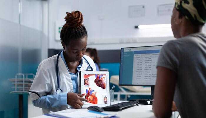 Diagnosis and monitoring - tycoonstory | tycoonstory media The doctor explains hypertension and heart disease, using a heart diagram on a digital tablet to a patient in a clinical setting.