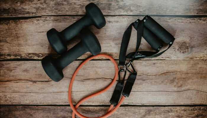 Ease of use - tycoonstory | tycoonstory media Including a pair of black dumbbells and an orange resistance band with handles, laid out on a wooden surface. It highlights exercise tools, particularly the resistance band, for workout routines or home gym setups