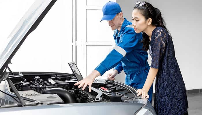 Evaluating customer service and communication - tycoonstroy | tycoonstory media Mechanic explaining car repair details to a customer at an auto repair shop in san francisco, with the car hood open and diagnostic tools in use