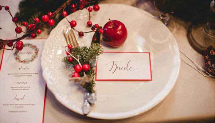 Festive wedding in red and gold - tycoonstory | tycoonstory media Wedding themes perfect for winter festive wedding table setting with a white plate red apple evergreen sprigs red berries and a handwritten bride place card