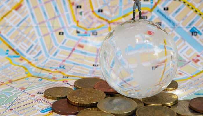 Geographic diversification in a globalized world - tycoonstory | tycoonstory media A miniature figure standing on a globe, surrounded by coins, symbolizing the future of diversification and global investment strategies