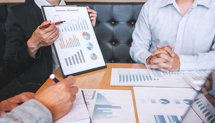 Get help from important services - tycoonstory | tycoonstory media Professionals discussing data visualizations on a clipboard and documents on a table, related to selling a recruitment business