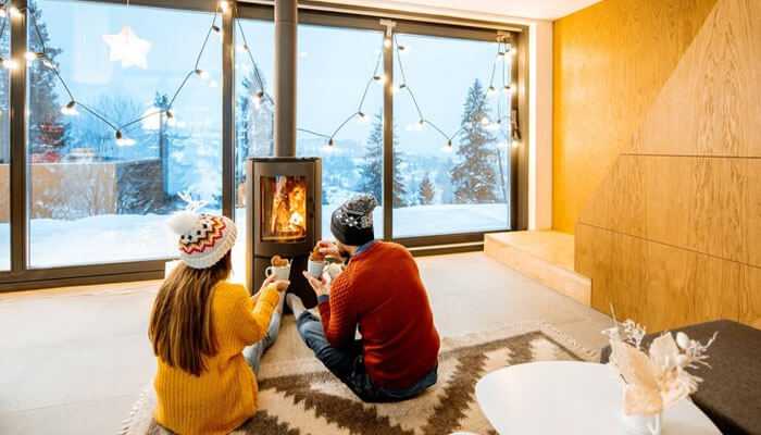 Get outside often - tycoonstory | tycoonstory media A couple sits next to a fireplace in a cozy room, enjoying hot drinks and a warm atmosphere as they transition smoothly into winter.