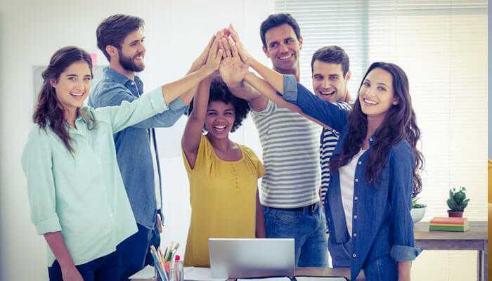 Get the right team in your corner - tycoonstory | tycoonstory media A team of diverse aspiring entrepreneurs celebrating success with a group high-five in a bright office setting.