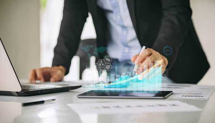 Go electronic in your marketing - tycoonstory | tycoonstory media A professional interacting with a tablet displaying a holographic upward graph, symbolizing real estate transactions and business growth