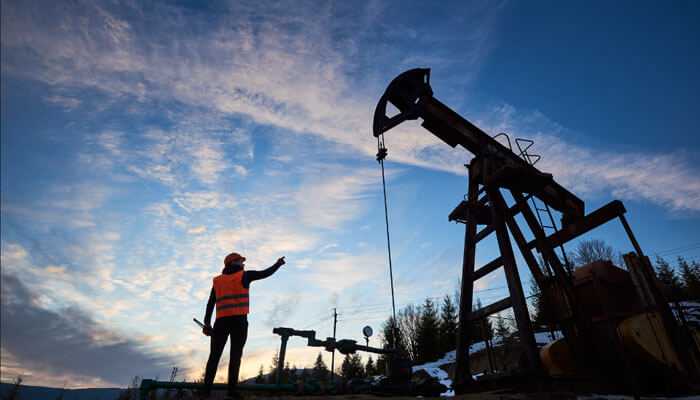 High pressure capability - tycoonstory | tycoonstory media Silhouette of a worker in a safety vest pointing at an industrial grade pumps at sunset. Sky is cloudy with trees in the background.