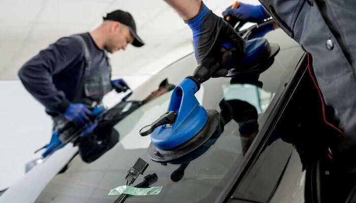 How to find reliable windshield repair services near you - tycoonstory | tycoonstory media Two technicians using suction tools to install or repair a car windshield, illustrating windshield repair costs in burlington.