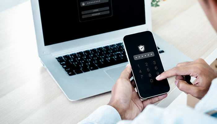 How to get a temporary phone number for verification - tycoonstory | tycoonstory media Person using a smartphone with a temporary phone number for verification, with a laptop displaying a login screen in the background, symbolizing digital identity protection