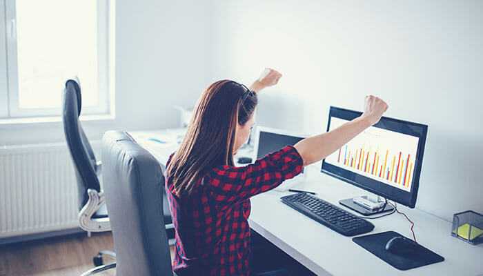 How women are breaking barriers - tycoonstory | tycoonstory media Women in hedge funds as a woman celebrates success at her desk, viewing a positive chart on her computer, signifying achievement and progress in finance or data analysis.