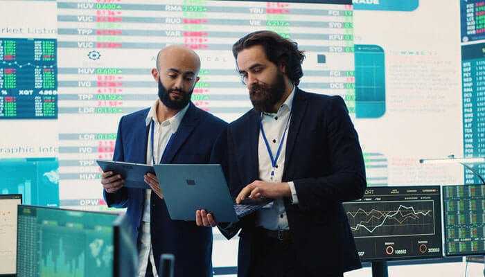 Mitigating the impact of biases and emotions - tycoonstory | tycoonstory media Business professionals reviewing financial data on a laptop discuss decision making in hedge funds with the stock charts in the background.