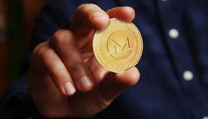 Monero - tycoonstory | tycoonstory media A person holding a gold monero coin with the monero logo, symbolizing investment in privacy coins and digital currency.