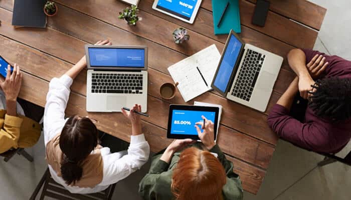 Neglect of marketing and user acquisition strategies - tycoonstory | tycoonstory media Team working on laptops and tablets around big, wooden table; on screen building your first mobile app.