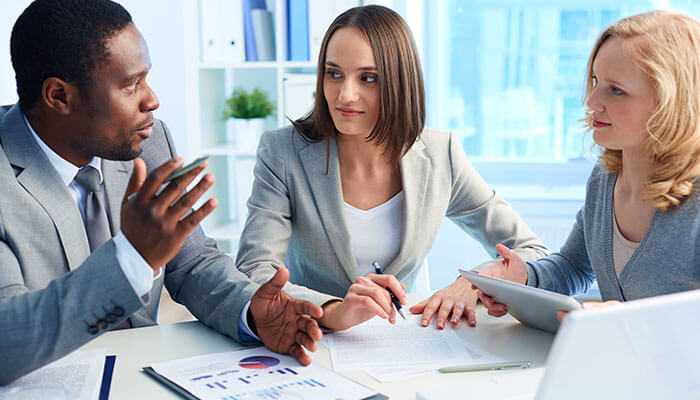 Personalized learning for business leaders - tycoonstory | tycoonstory media Group of business professionals discussing a custom-paced degree program, collaborating and strategizing at a table with documents and a tablet, representing teamwork and business planning