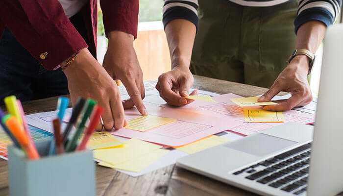 Practical applications in the workplace - tycoonstory | tycoonstory media Behavioral therapy transforms leaders as collaborative team brainstorming session with hands organizing sticky notes and papers on a table, symbolizing structured planning and strategic thinking