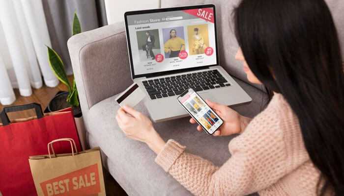 Product add-ons for woocommerce - tycoonstory | tycoonstory media Customer shopping online with woocommerce plugins on a laptop and smartphone, browsing a fashion stores sale section with shopping bags nearby, representing an enhanced ecommerce experience
