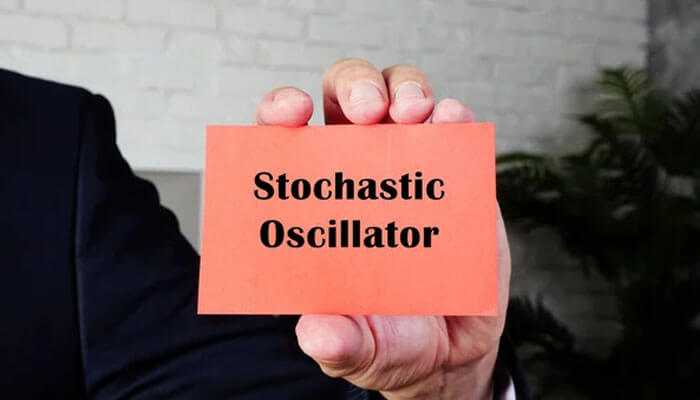 Pros and cons of using the stochastic oscillator - tycoonstory | tycoonstory media Hand holding an orange card with the text'Stochastic Oscillator', symbolizing settings for technical trading analysis.
