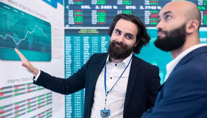 Recency bias the influence of recent events on future expectations - tycoonstory | tycoonstory media Two financial analysts discus the stock market data on the screen, analyze behavioral traps, pointing to a chart in a modern trading room.