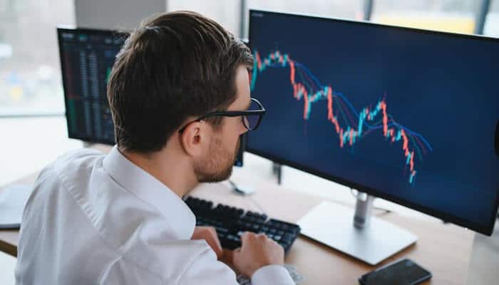 Risks to consider in stocks and demat accounts - tycoonstory | tycoonstory media Various monitors with candlestick charts showing stock market data being analyzed by a man to study the trends for investment decisions.