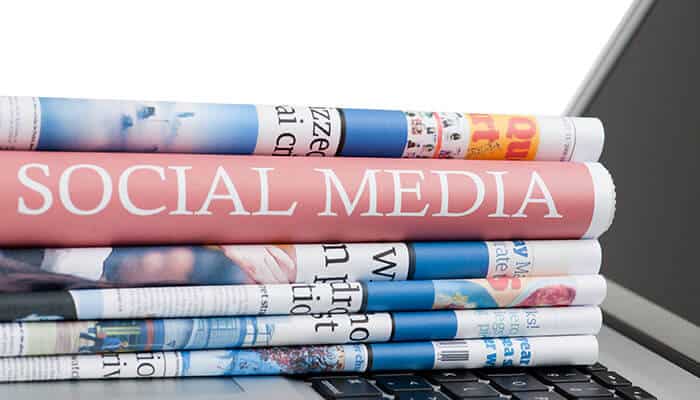 Social media detective work - tycoonstory | tycoonstory media Dmwin with a stack of rolled-up newspapers featuring social media prominently on the top one, placed on a laptop keyboard