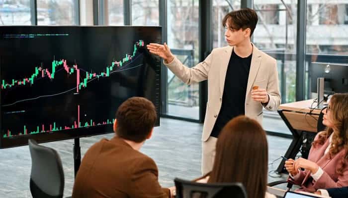 Thorough educational resources - tycoonstory | tycoonstory media A forex trading broker explaining market trends and charts to a group of traders during a strategy session