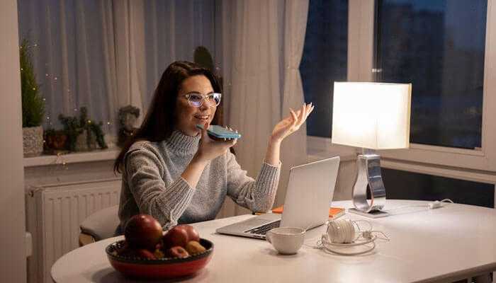 Thrive in your new role - tycoonstory | tycoonstory media Woman working from home representing the shift from freelancer to full-time remote engineer, using voice commands, and a laptop.