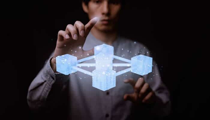 Top blockchain certifications for professional growth - tycoonstory | tycoonstory media A person interacting with a holographic representation of interconnected digital cubes, symbolizing blockchain careers and technology, against a dark background