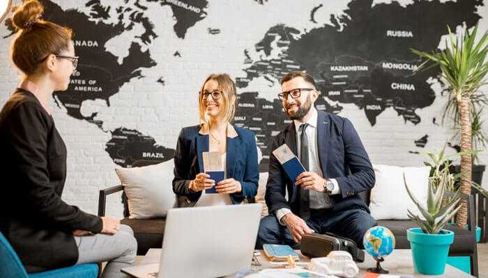 Understanding the range of offered services - tycoonstory | tycoonstory media Smiling clients holding passports while discussing travel plans with a travel management company agent in a very stylish office.