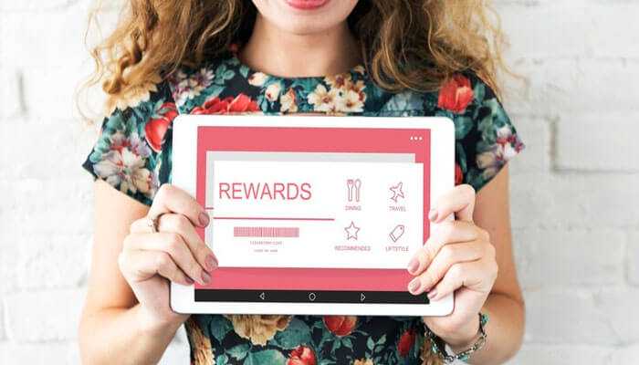 User-friendly experience and rewards - tycoonstory | tycoonstory media Tiranga app with a woman holding a tablet displaying a rewards program interface featuring categories like dining, travel, and lifestyle, along with a progress bar