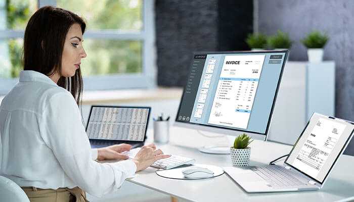 Visibility with e-invoice reports - tycoonstory | tycoonstory media Businesswoman using accounting software pairs with e-invoicing on multiple screens, representing digital transformation and efficiency in managing invoices and finances.